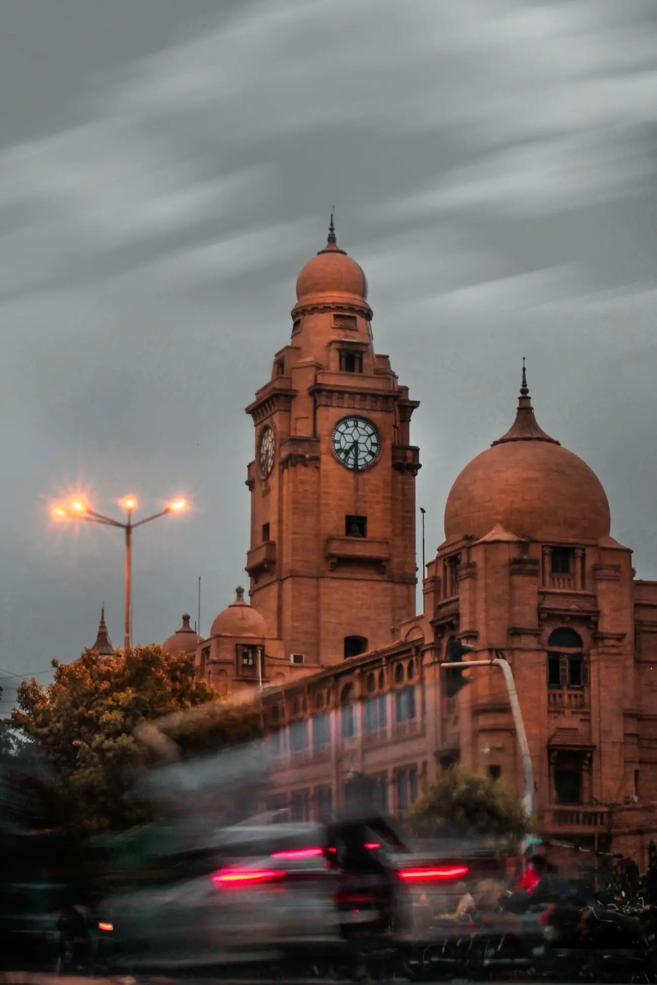 A historic Karachi clock tower lit up at dusk with traffic passing below